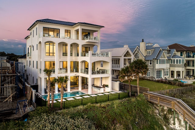 back house at dusk with a fenced in pool, a patio, and a balcony