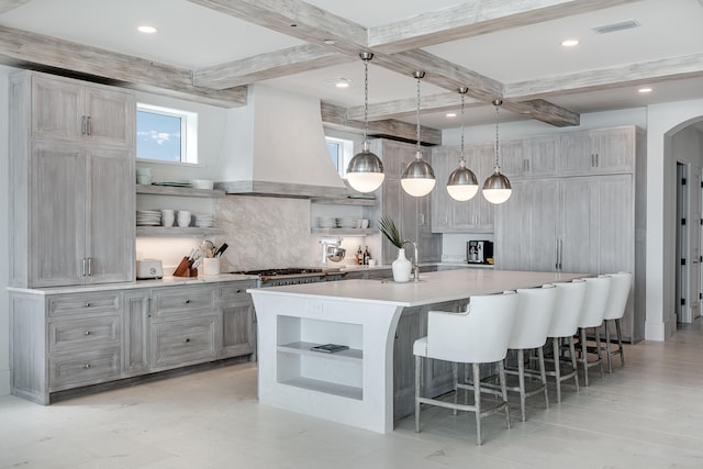 kitchen with wall chimney exhaust hood, pendant lighting, tasteful backsplash, beam ceiling, and a large island