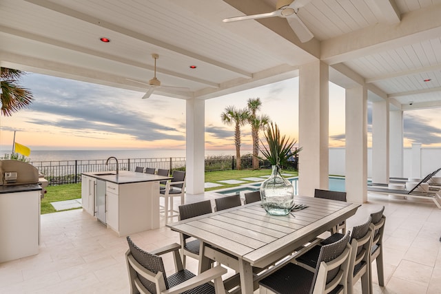 patio terrace at dusk featuring a water view, a fenced in pool, sink, and ceiling fan