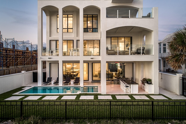 back house at dusk featuring a balcony, a fenced in pool, a yard, and a patio area