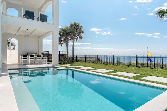 view of swimming pool featuring a water view, a patio, a yard, ceiling fan, and a bar