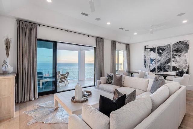 living room with a water view, light hardwood / wood-style flooring, a wealth of natural light, and ceiling fan