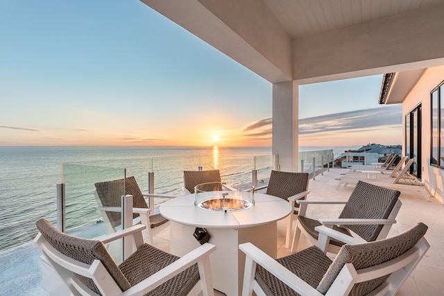 balcony at dusk featuring a water view and an outdoor living space with a fire pit