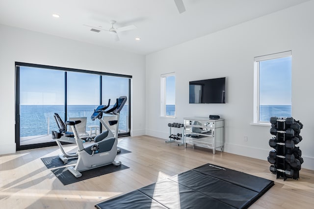 exercise area with a water view, wood-type flooring, a wealth of natural light, and ceiling fan