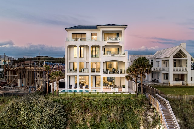 back house at dusk with a fenced in pool, a patio, and a balcony