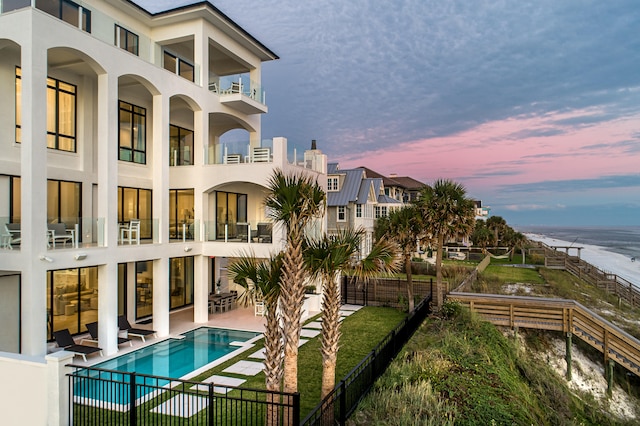 back house at dusk with a water view, a fenced in pool, a balcony, and a patio area