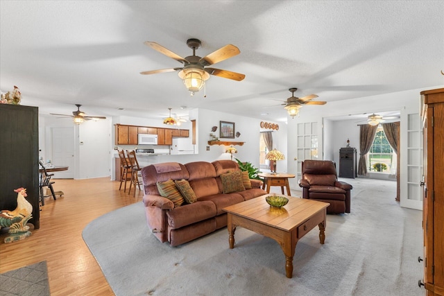 living room featuring ceiling fan, a textured ceiling, and light wood-type flooring