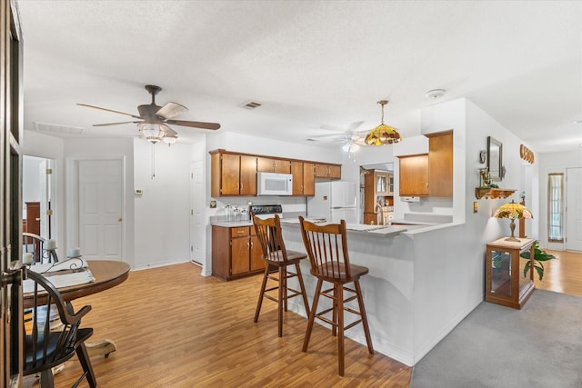 kitchen featuring light wood-type flooring, white appliances, a kitchen breakfast bar, kitchen peninsula, and a textured ceiling