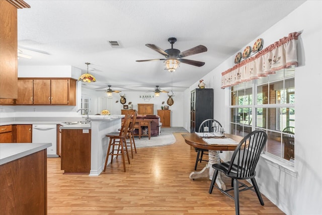 kitchen with light wood-type flooring, sink, kitchen peninsula, decorative light fixtures, and a kitchen breakfast bar