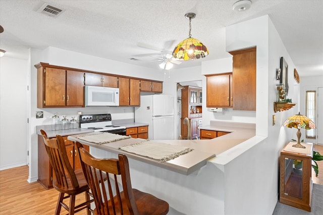 kitchen with light hardwood / wood-style floors, white appliances, decorative light fixtures, a kitchen bar, and a textured ceiling