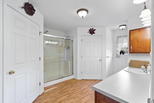 bathroom with hardwood / wood-style flooring, a shower with door, vanity, and a textured ceiling