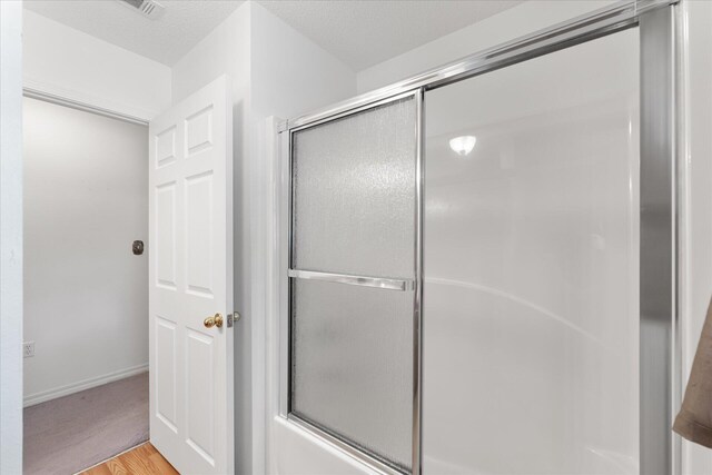 bathroom with enclosed tub / shower combo, hardwood / wood-style flooring, and a textured ceiling