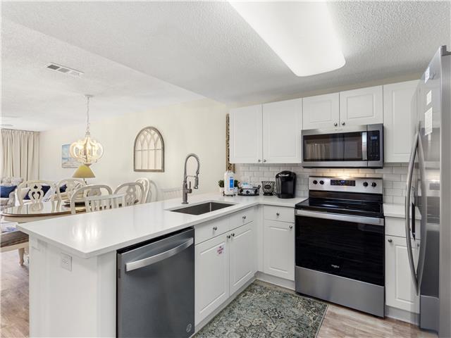 2076 Scenic Gulf Dr Unit 1013, Miramar Beach, FL 32550 - kitchen with visible vents, a peninsula, a textured ceiling, a sink, and stainless steel appliances