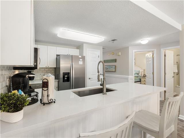 2076 Scenic Gulf Dr Unit 1013, Miramar Beach, FL 32550 - kitchen featuring a peninsula, a textured ceiling, white cabinetry, stainless steel fridge with ice dispenser, and a sink