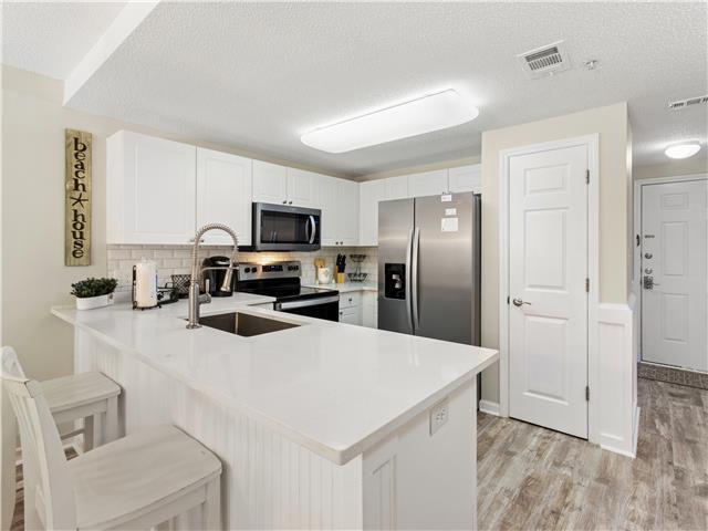 2076 Scenic Gulf Dr Unit 1013, Miramar Beach, FL 32550 - kitchen with appliances with stainless steel finishes, a sink, light wood-style flooring, a peninsula, and backsplash