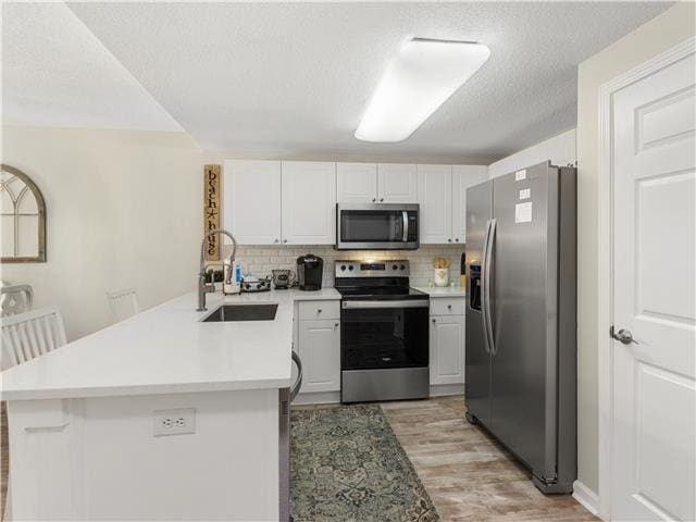 2076 Scenic Gulf Dr Unit 1013, Miramar Beach, FL 32550 - kitchen with appliances with stainless steel finishes, tasteful backsplash, a sink, a peninsula, and light wood-style flooring