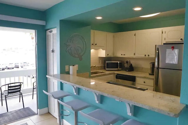 kitchen with appliances with stainless steel finishes, kitchen peninsula, light stone countertops, and a kitchen bar