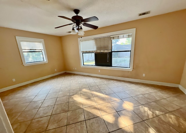 tiled empty room featuring ceiling fan, a textured ceiling, and a healthy amount of sunlight