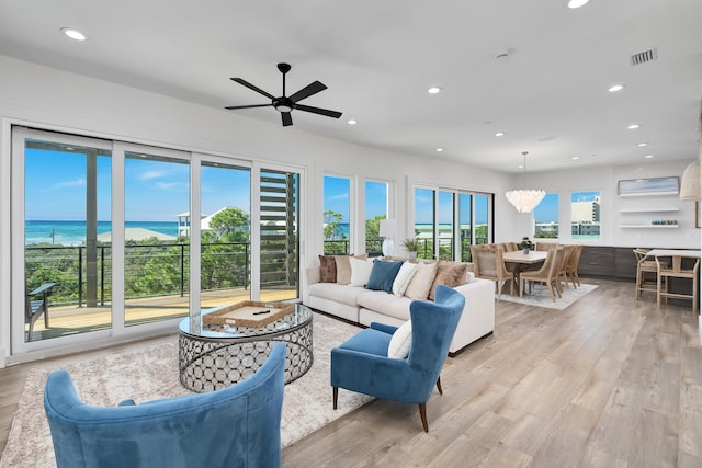 living room with light hardwood / wood-style flooring, a water view, and ceiling fan with notable chandelier