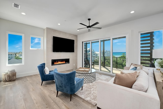 living room with light hardwood / wood-style floors, a large fireplace, and ceiling fan