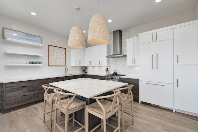 kitchen with wall chimney range hood, white cabinets, dark brown cabinets, hanging light fixtures, and light hardwood / wood-style floors