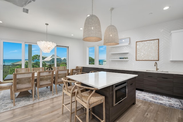 kitchen with dark brown cabinets, light hardwood / wood-style flooring, sink, decorative light fixtures, and a center island