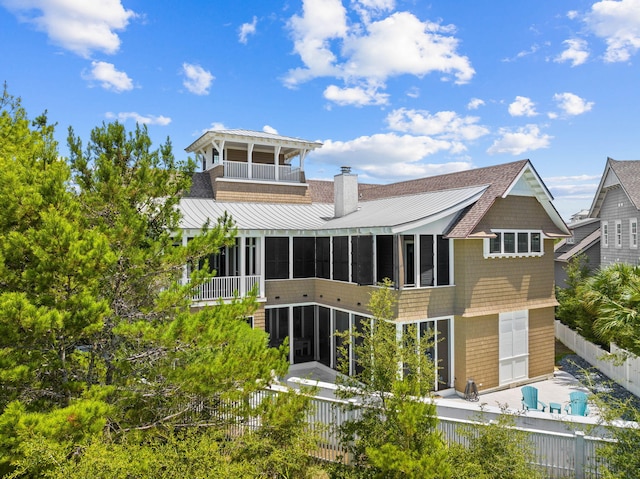 back of house with a balcony, a sunroom, a fenced backyard, a chimney, and a standing seam roof