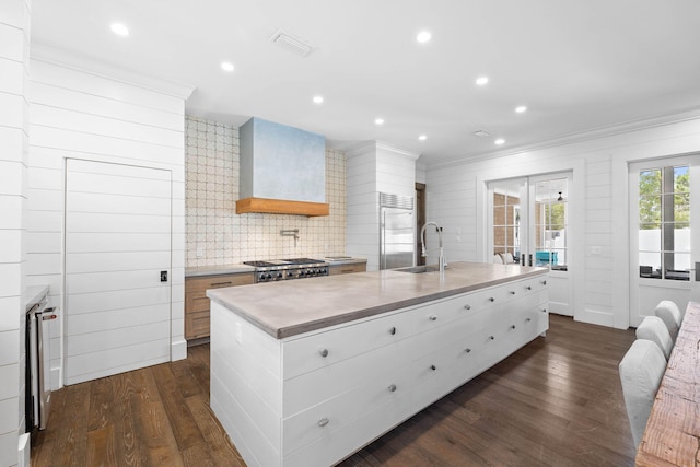 kitchen with custom exhaust hood, dark hardwood / wood-style floors, an island with sink, appliances with stainless steel finishes, and white cabinetry