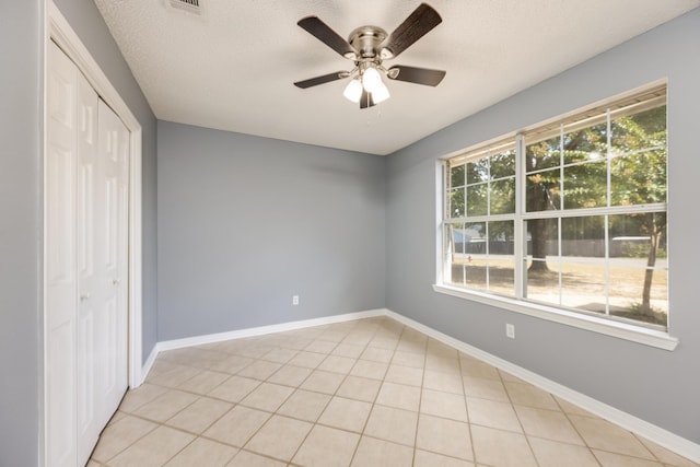 unfurnished bedroom featuring ceiling fan, a closet, light tile patterned floors, and a textured ceiling