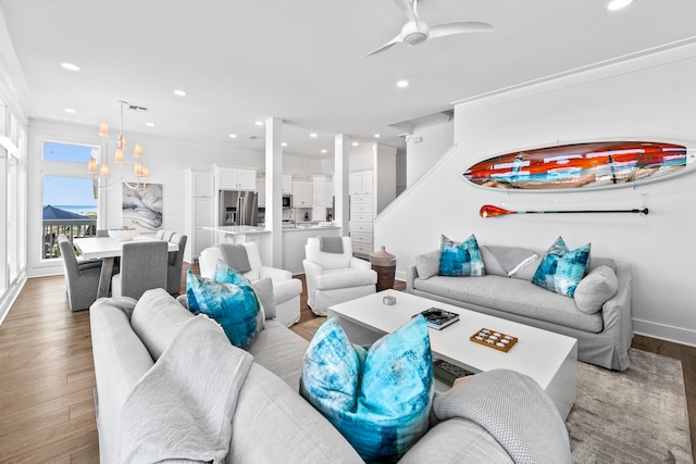 living room with ceiling fan with notable chandelier, hardwood / wood-style floors, and ornamental molding