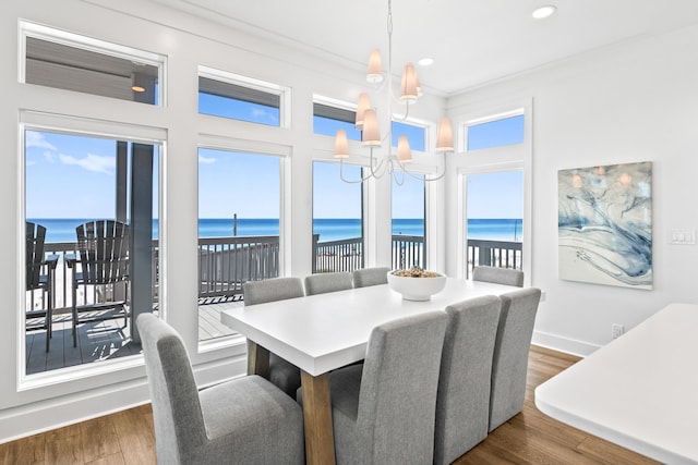 dining room with a water view, an inviting chandelier, ornamental molding, and dark hardwood / wood-style flooring