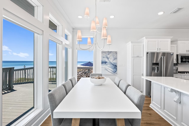 dining area featuring a notable chandelier, crown molding, dark hardwood / wood-style flooring, and a water view