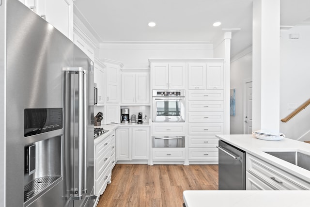 kitchen with ornamental molding, appliances with stainless steel finishes, light hardwood / wood-style floors, and white cabinetry