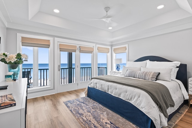 bedroom with a water view, a raised ceiling, hardwood / wood-style floors, and ceiling fan