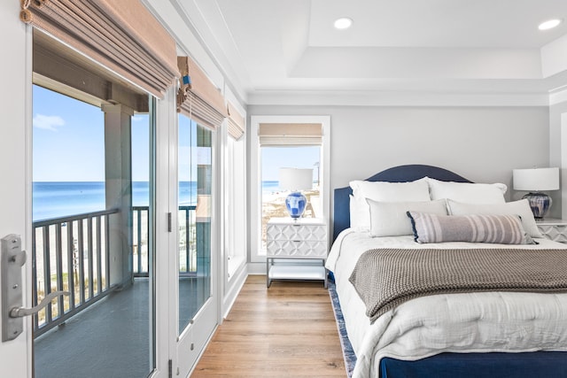 bedroom featuring a beach view, hardwood / wood-style flooring, a tray ceiling, access to exterior, and a water view