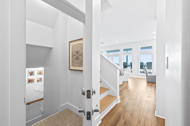 stairs with wood-type flooring and crown molding