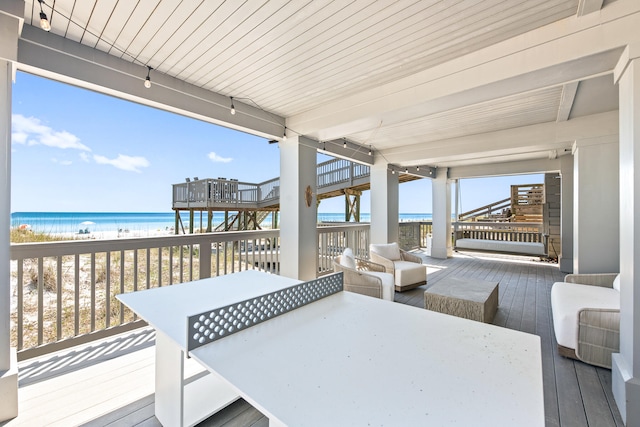 wooden deck with an outdoor living space, a water view, and a view of the beach