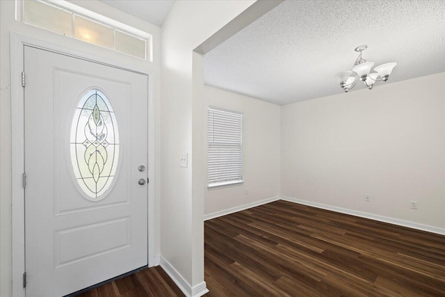 foyer featuring dark wood-type flooring, an inviting chandelier, and a textured ceiling