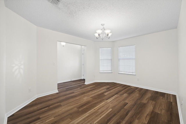 spare room with an inviting chandelier, dark hardwood / wood-style floors, and a textured ceiling