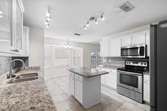 kitchen featuring sink, light stone countertops, appliances with stainless steel finishes, a center island, and white cabinetry