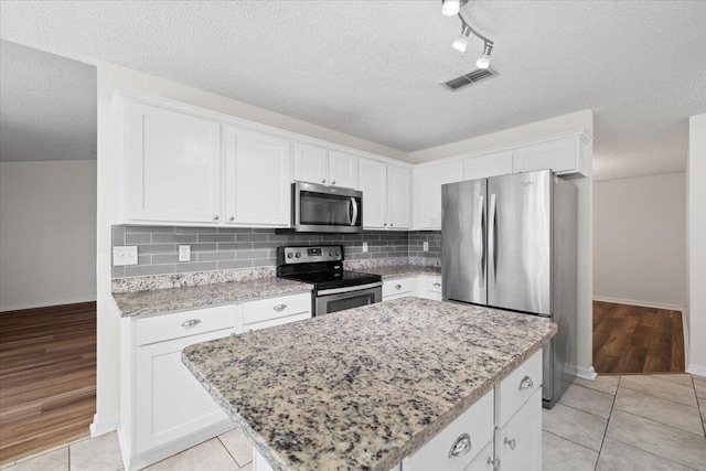 kitchen with stainless steel appliances, white cabinets, a kitchen island, and a textured ceiling