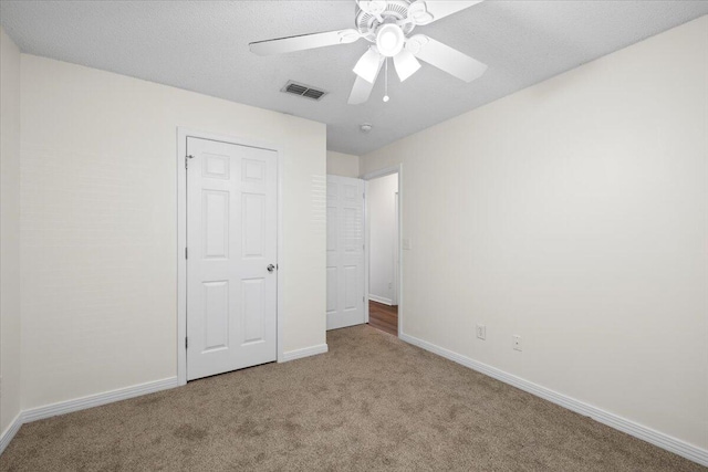 unfurnished bedroom featuring light colored carpet, a textured ceiling, and ceiling fan