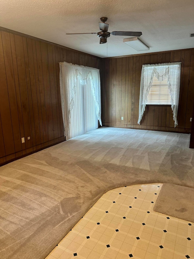 spare room with ceiling fan, carpet floors, wooden walls, and a textured ceiling