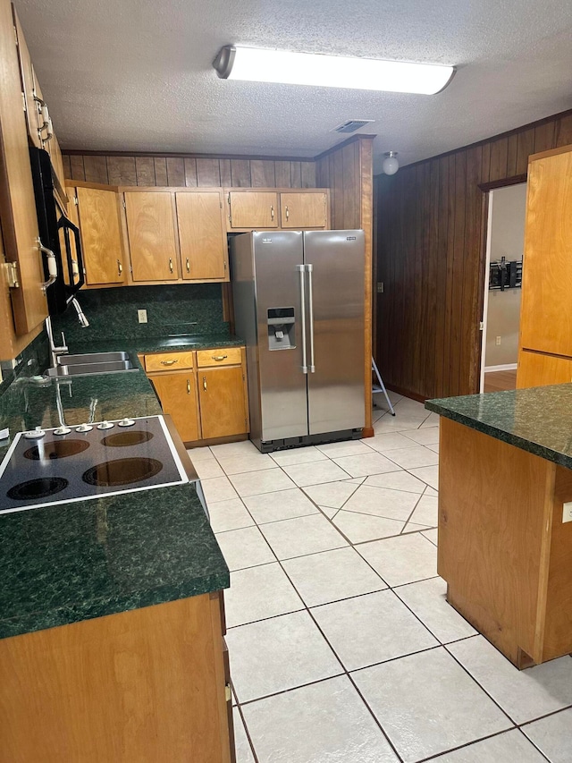 kitchen with wood walls, stainless steel fridge, decorative backsplash, light tile patterned floors, and a textured ceiling