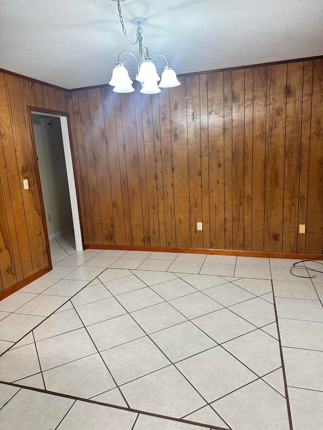 unfurnished dining area featuring wood walls, light tile patterned flooring, an inviting chandelier, and a textured ceiling