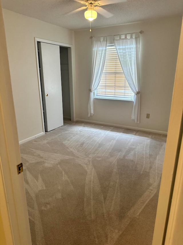 unfurnished bedroom featuring ceiling fan, a textured ceiling, a closet, and light carpet