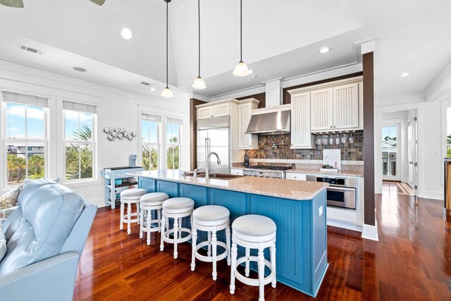 kitchen featuring a center island with sink, appliances with stainless steel finishes, decorative light fixtures, and dark hardwood / wood-style floors