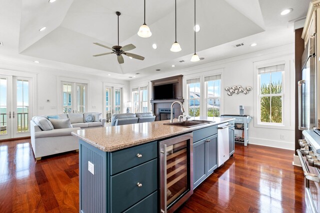 kitchen with a raised ceiling, a center island with sink, wine cooler, and sink