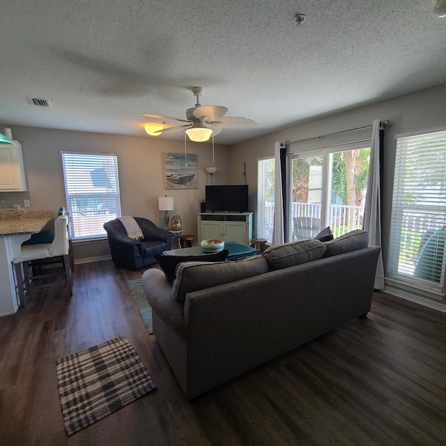 living room featuring ceiling fan, a textured ceiling, dark wood-type flooring, and a wealth of natural light