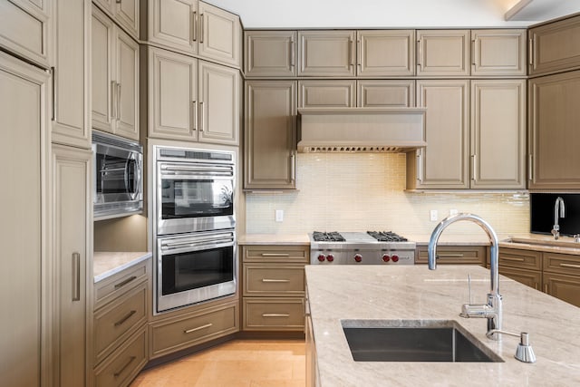 kitchen with sink, decorative backsplash, appliances with stainless steel finishes, light stone counters, and custom range hood